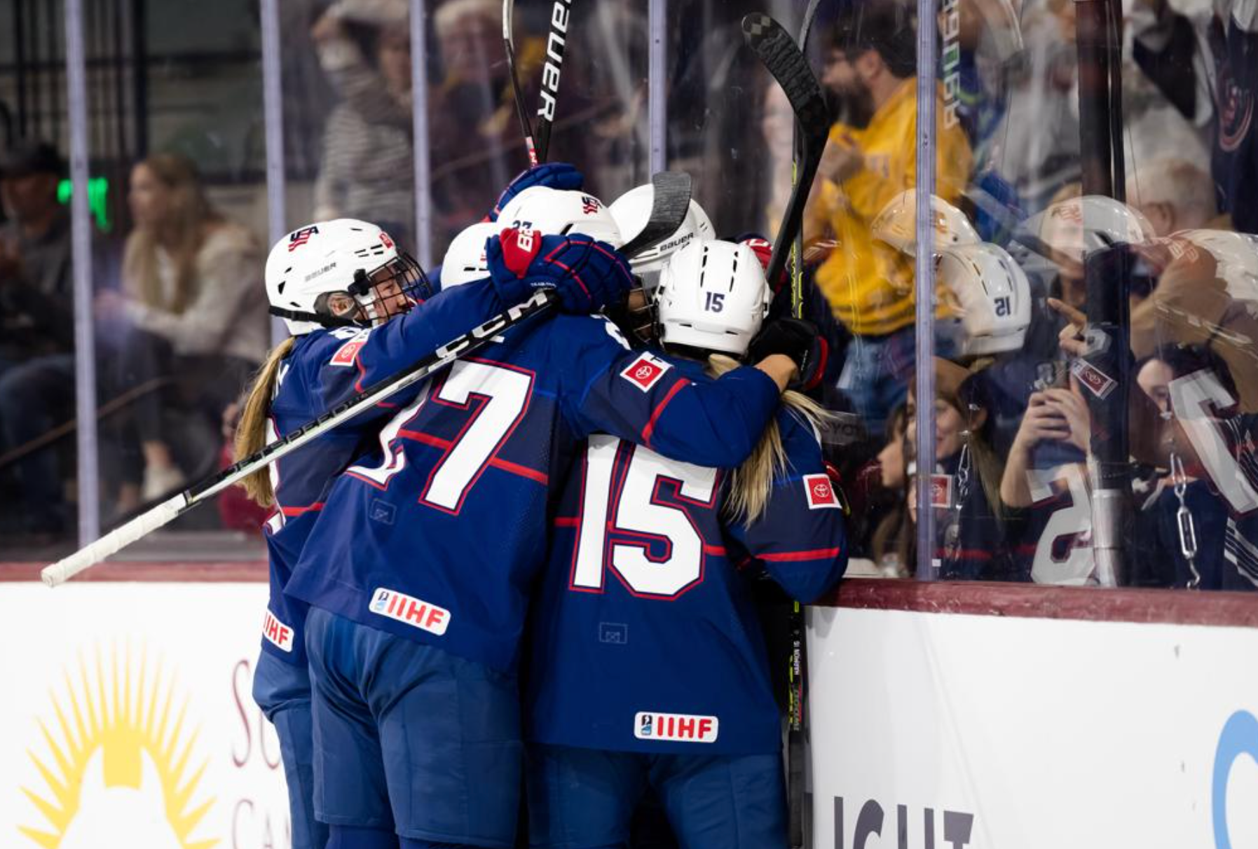 Members of the Team USA women's hockey team gather to celebrate while on the ice and wearing navy blue jerseys.