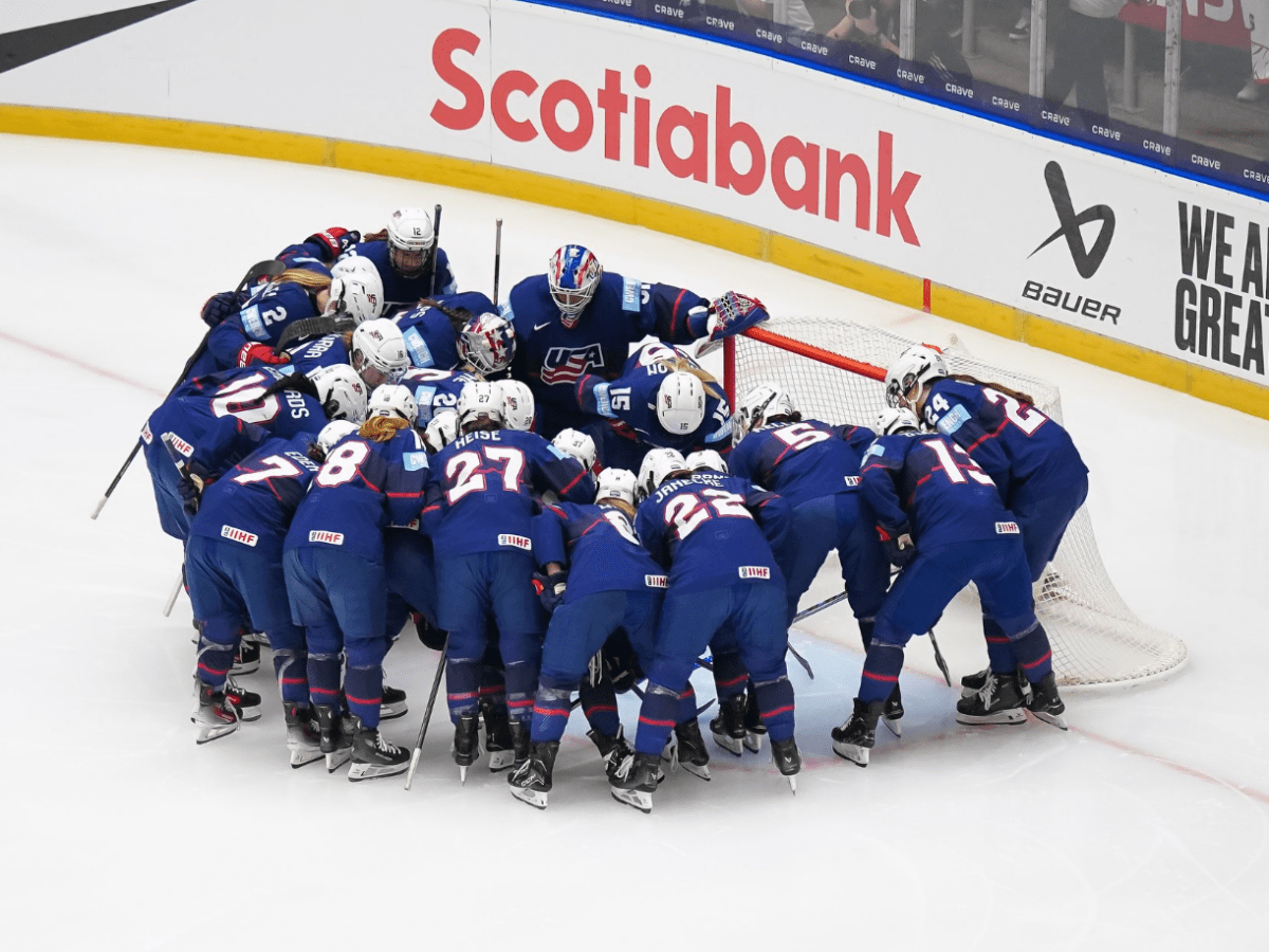Team USA forms a tight huddle around their crease before the game. They are all wearing blue home uniforms.