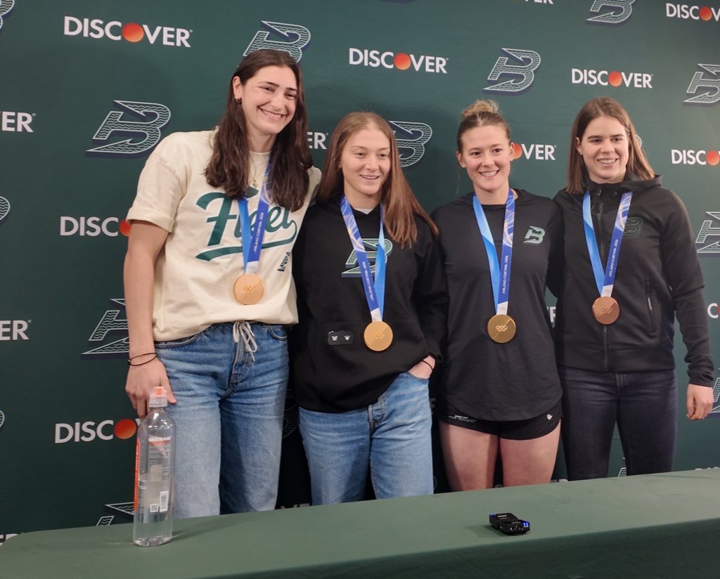 Megan Keller, Aerin Frankel, Haley Winn and Alina Müller smile at the camera while standing side by side wearing their Olympic medals.