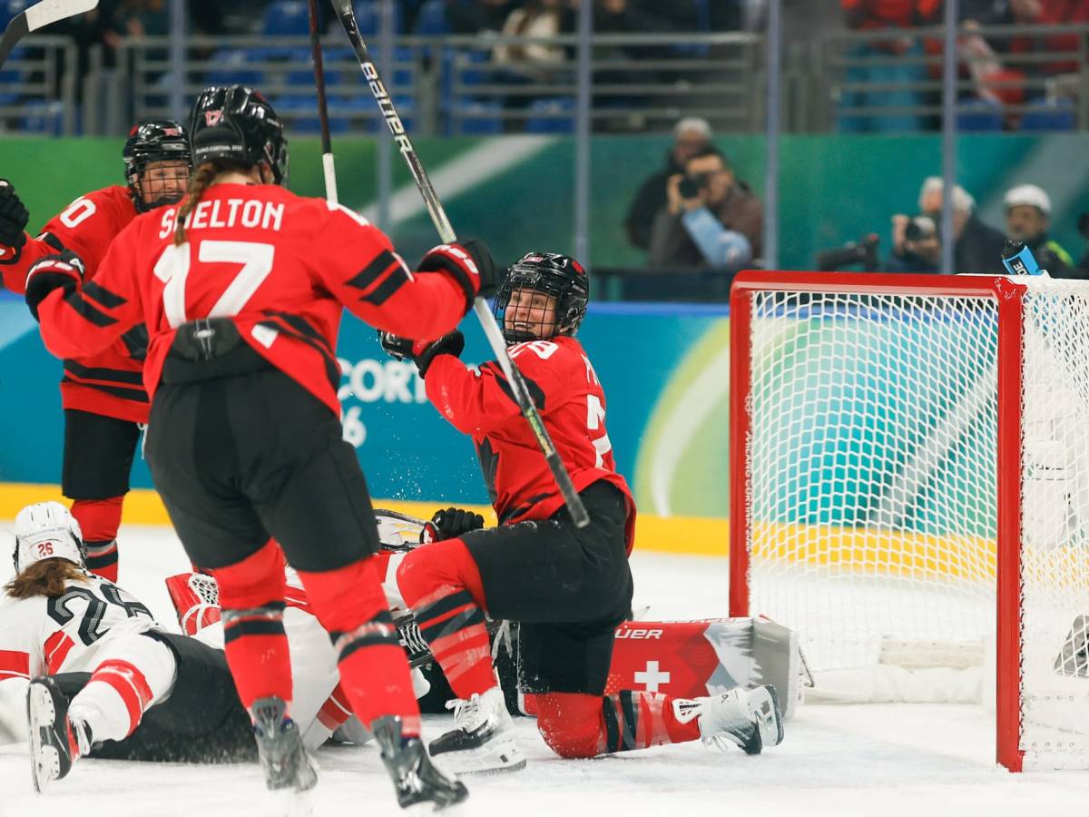 Marie Philip-Poulin is knelt down on one knee celebrating in front of the goal with her teammates.